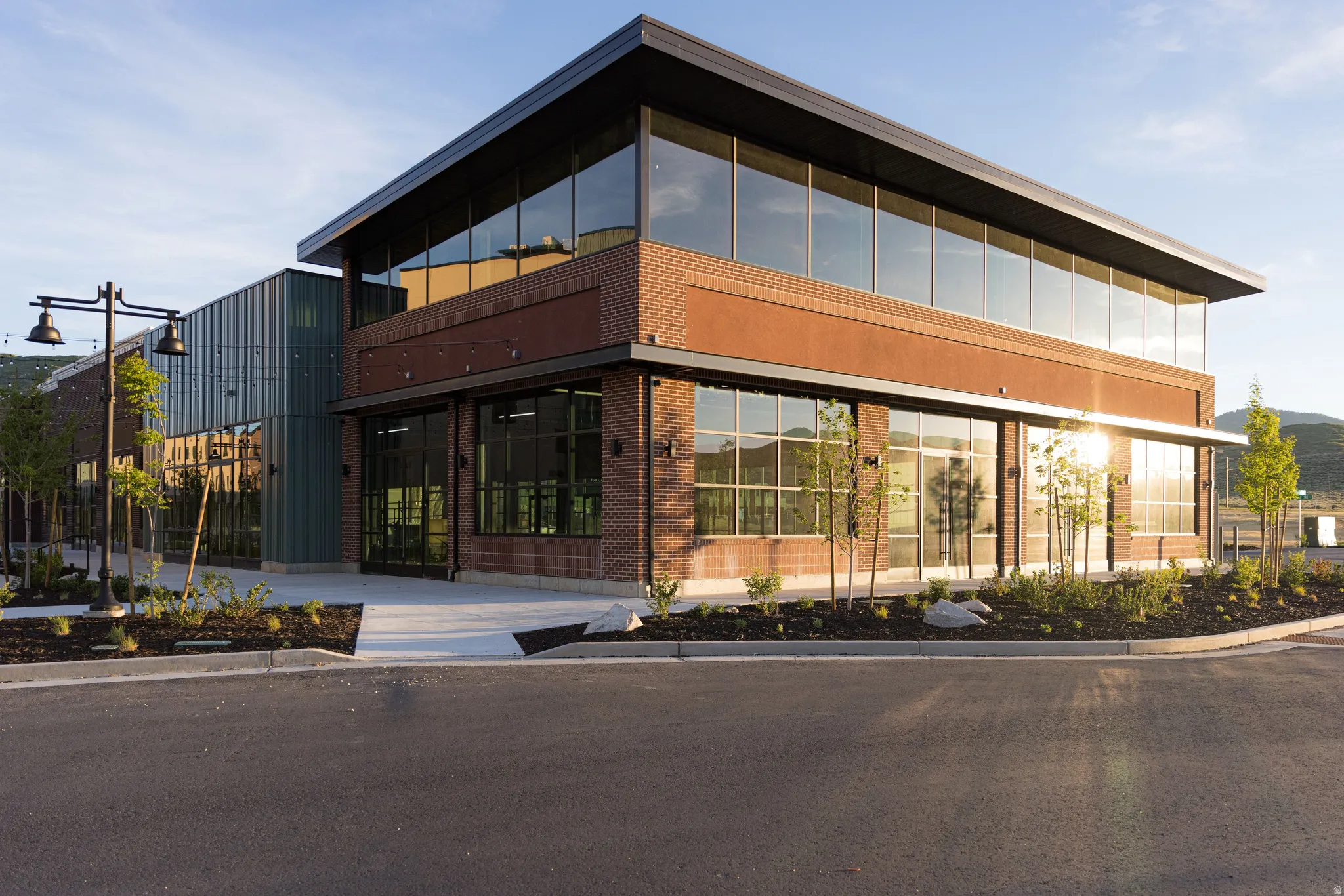 Contemporary commercial building featuring brick and metal panel exterior, expansive glass windows, a flat roofline, and landscaped planters