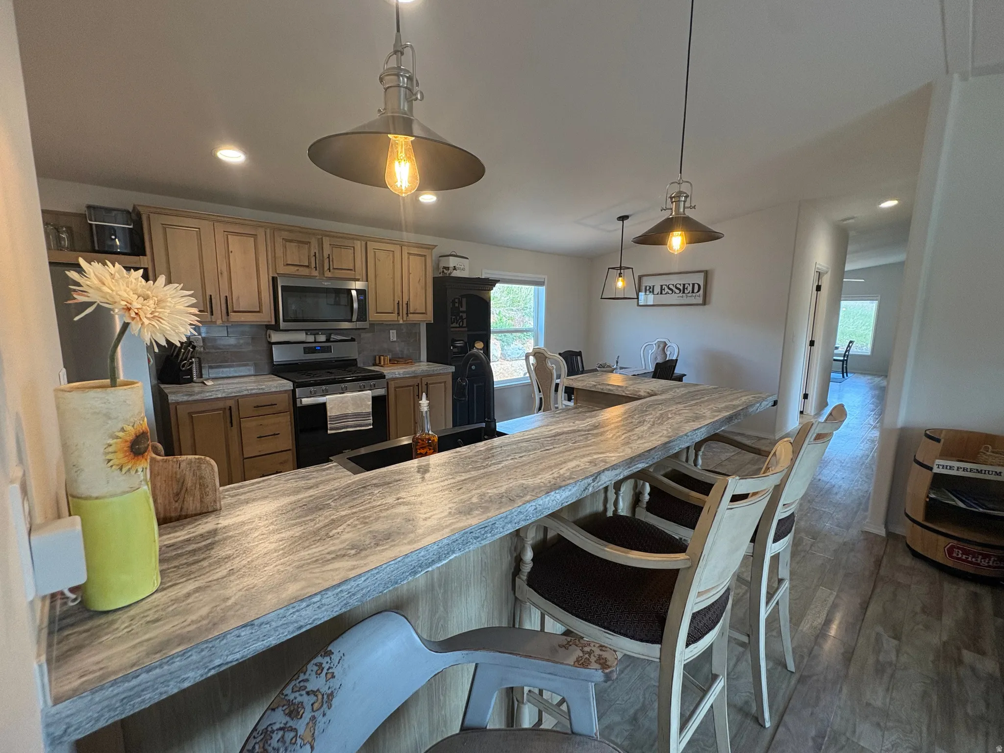 Kitchen featuring an extended island with a stone-finish countertop, light wood cabinetry, stainless steel appliances, and wood-finish flooring