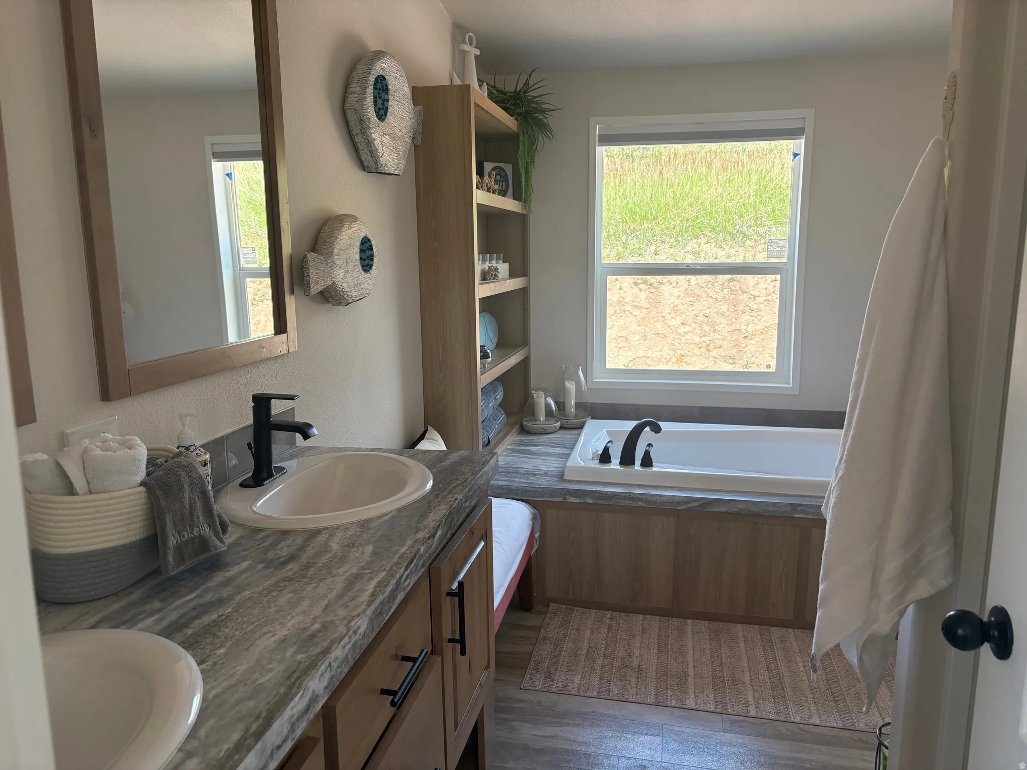 Bathroom featuring a built-in soaking tub, wood-finish vanity with dual sinks, and a framed mirror