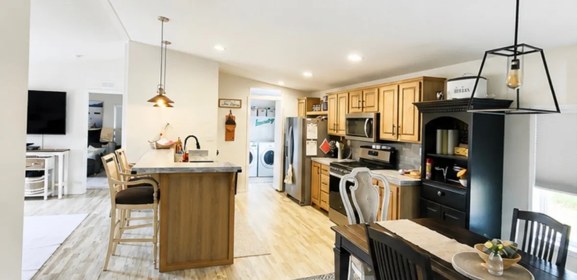 Open-concept kitchen featuring wood-finish flooring, light wood cabinetry, stainless steel appliances, a center island with seating, and recessed lighting