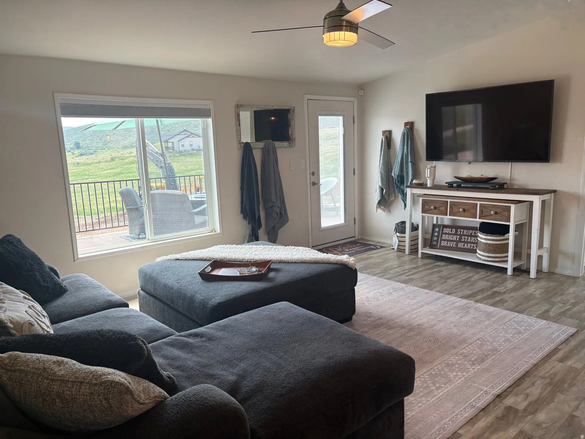 Living area featuring wood-finish flooring, a ceiling fan with integrated lighting, and a glass-paneled exterior door
