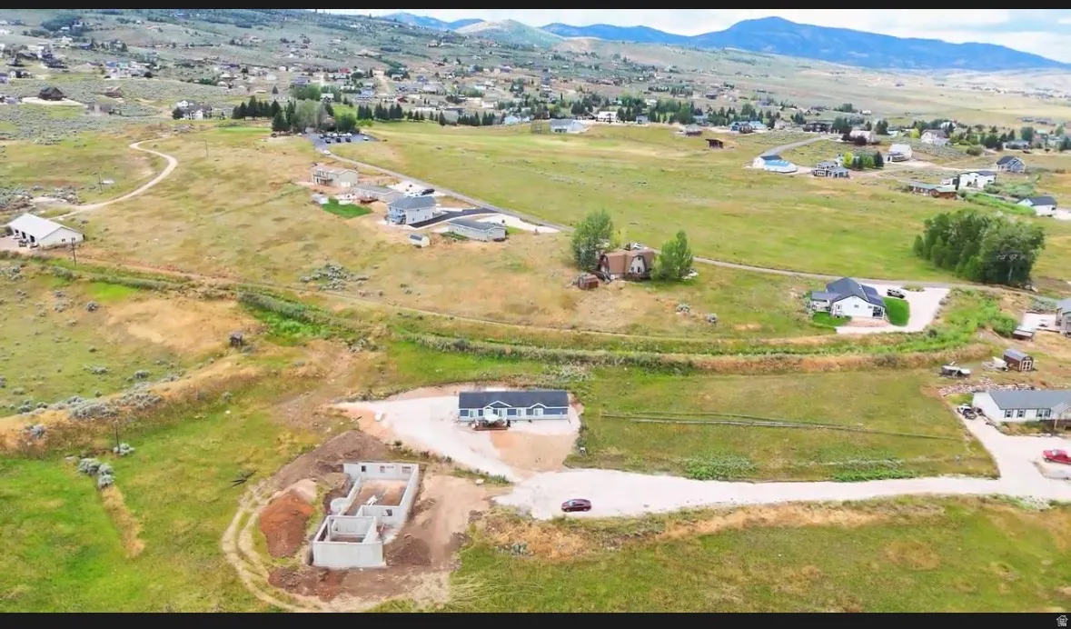 Expansive lot featuring a visible foundation for construction, surrounding open land, a partially developed residential area, and distant mountain scenery
