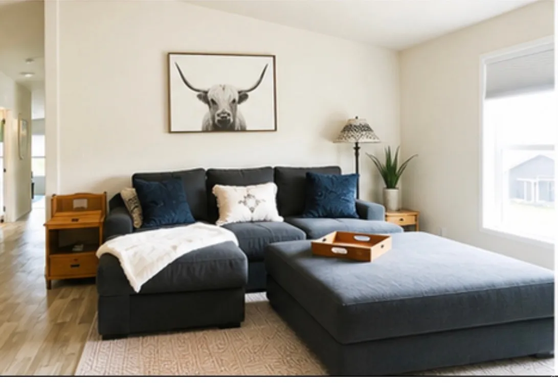 Spacious living area featuring light-toned walls, wood-finish flooring, and ample natural light from a large window