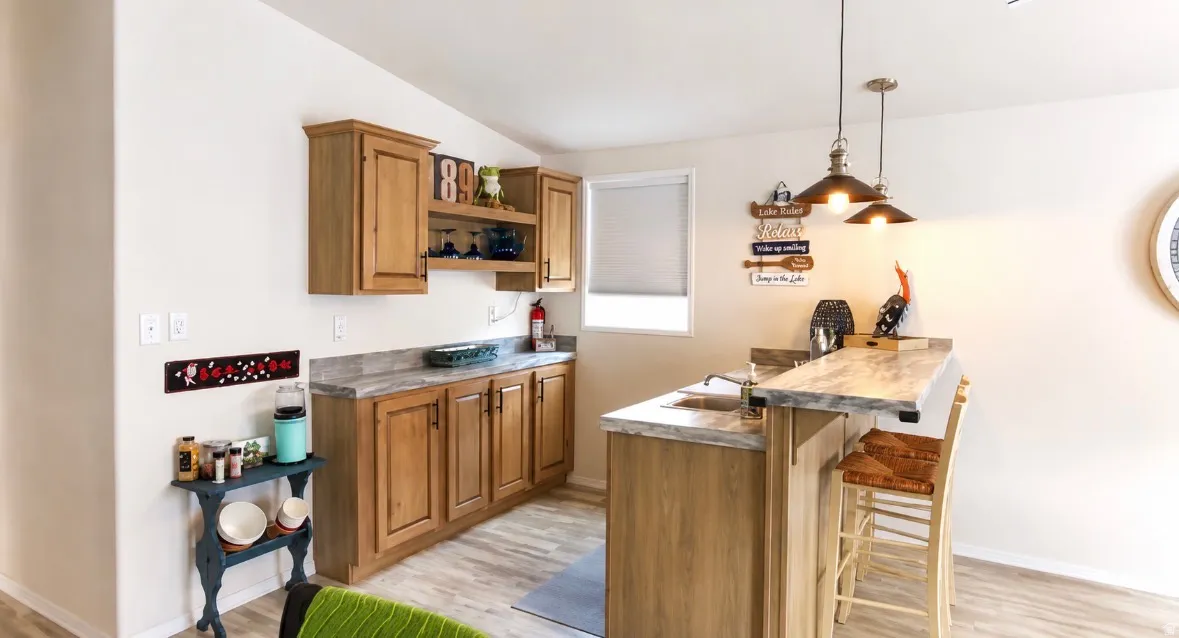 Built-in wet bar featuring wood cabinetry, stone-look countertops, an undermount sink, and pendant lighting fixtures