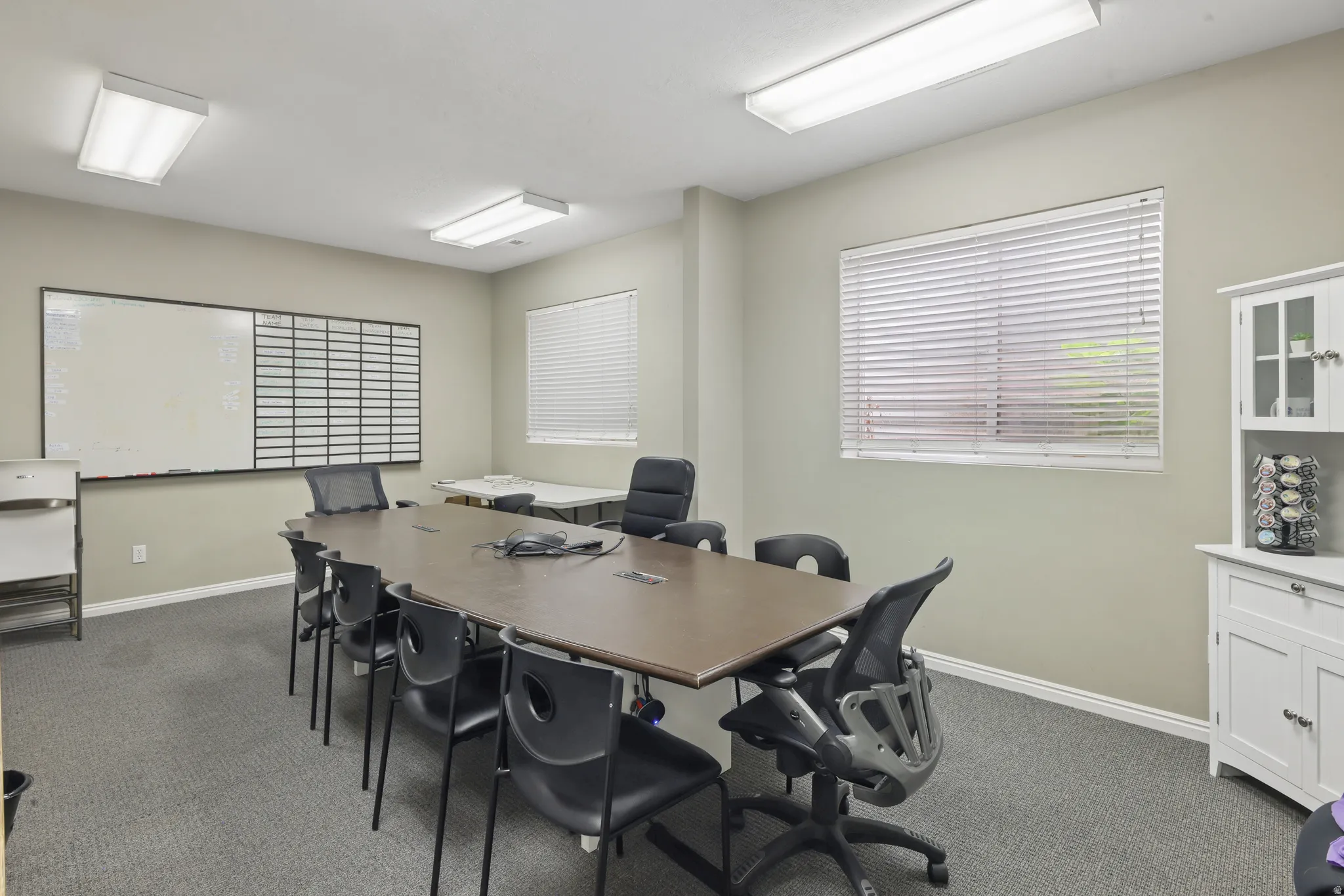 Conference room featuring neutral-toned walls, grey carpet, and overhead fluorescent lighting