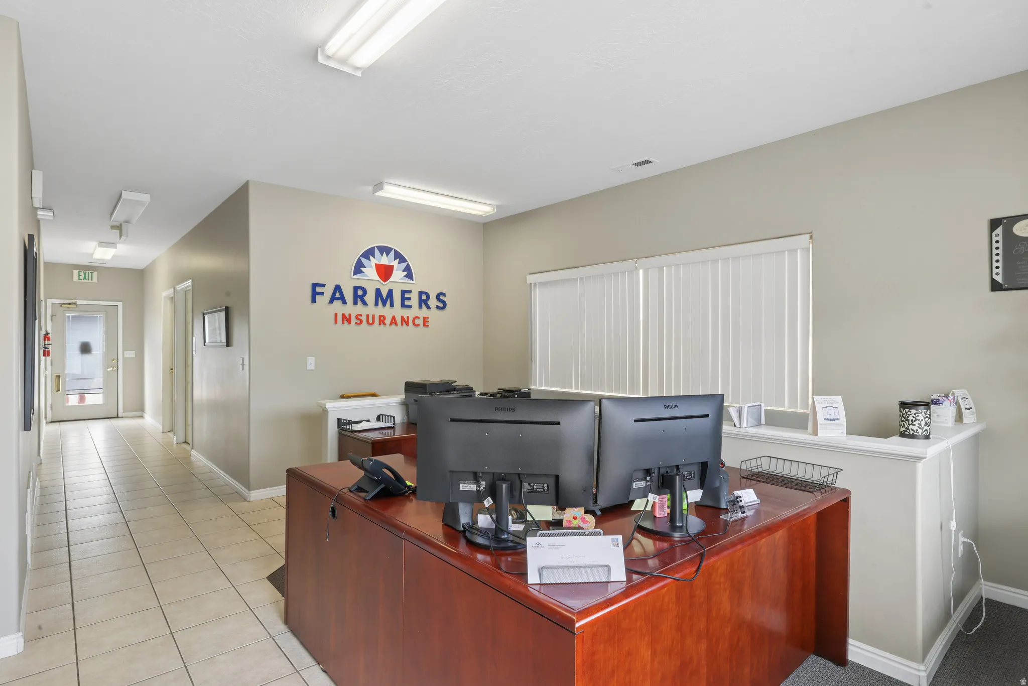 Open office area featuring a wood-finish reception desk, neutral wall tones, and recessed lighting