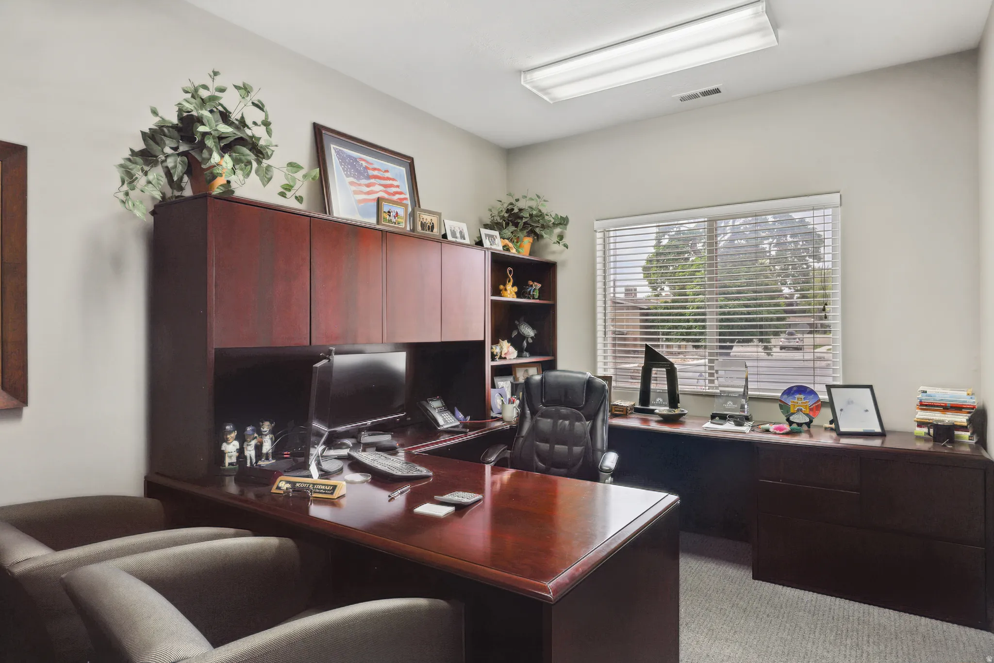 Office space featuring a large window with blinds, neutral wall paint, and carpet flooring