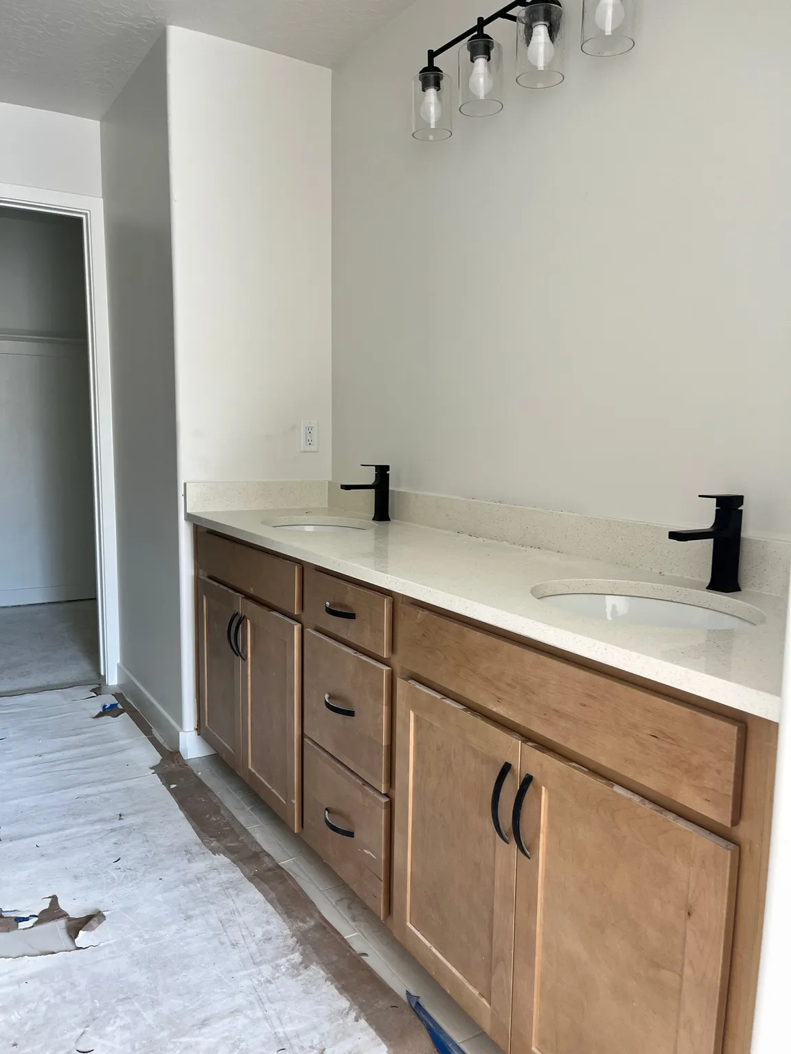 Double vanity featuring light wood-finish cabinetry with black hardware, white countertops, two undermount sinks, and two matte black faucets