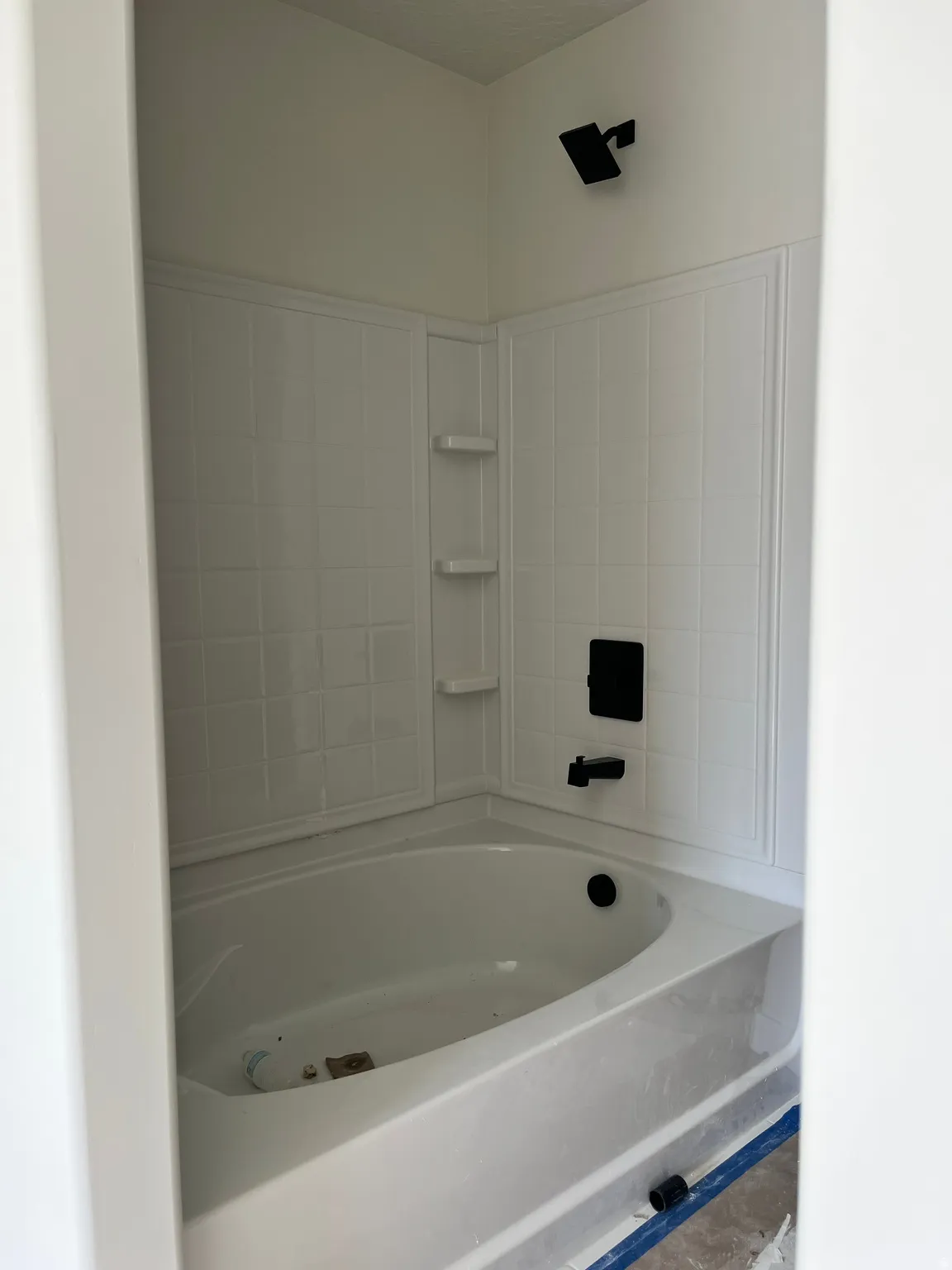 Corner bathtub with white tiled surround, integrated shelving, and matte black fixtures