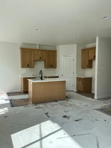 Kitchen featuring light wood cabinetry, white countertops, a central island with a sink, recessed lighting, and a white interior door