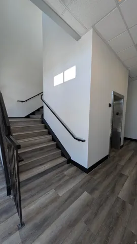 Stairwell featuring wood-finish flooring, dark metal handrails, and a stainless steel elevator