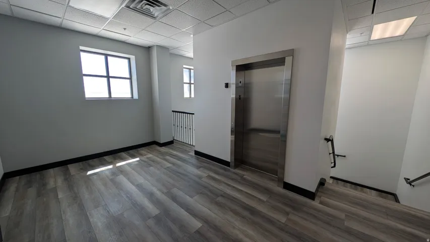Lobby area featuring wood-finish flooring, a stainless steel elevator, and a drop ceiling with recessed lighting