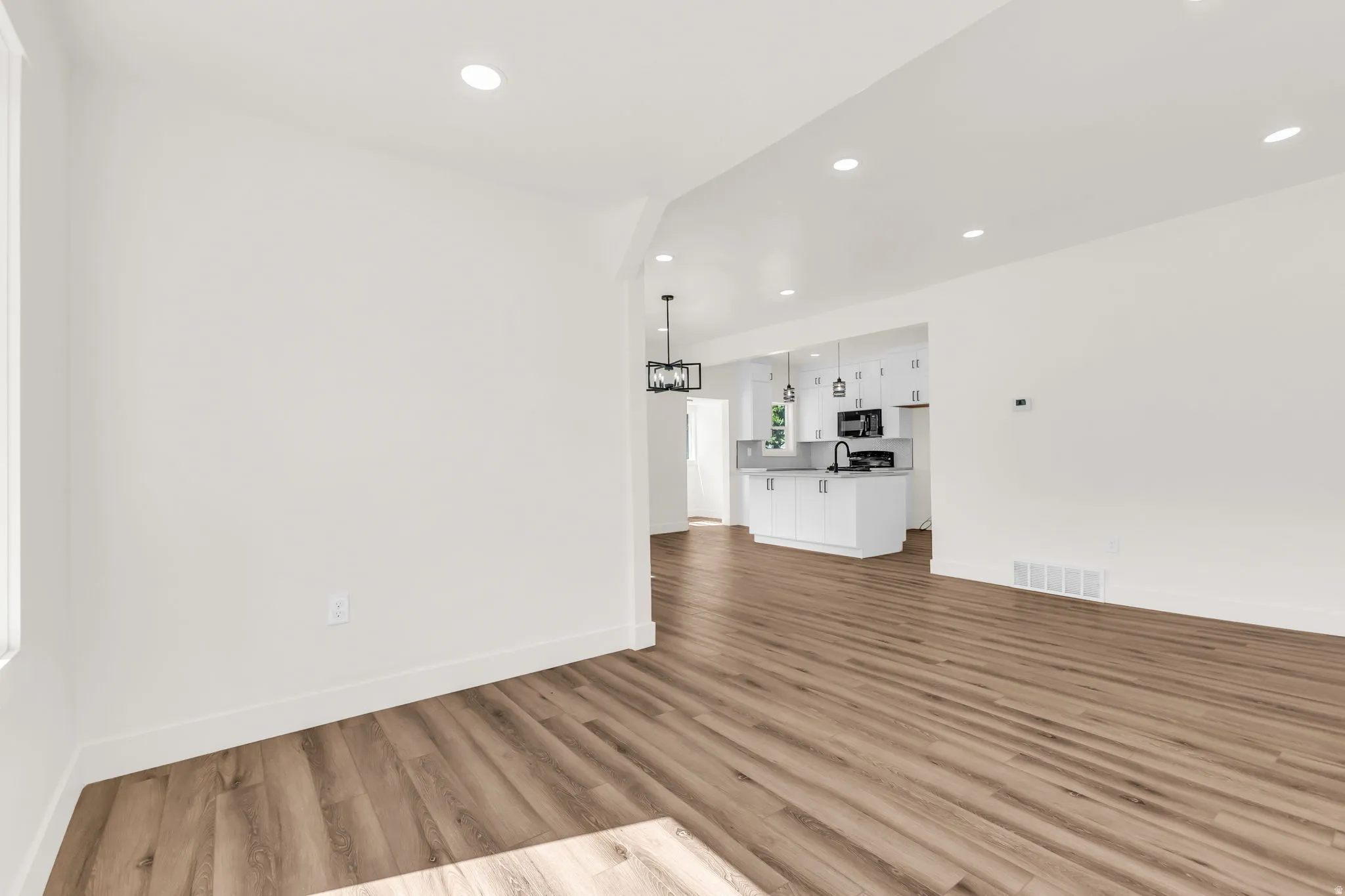 Spacious open-concept living area featuring wood-finish flooring, recessed lighting, and a white baseboard trim