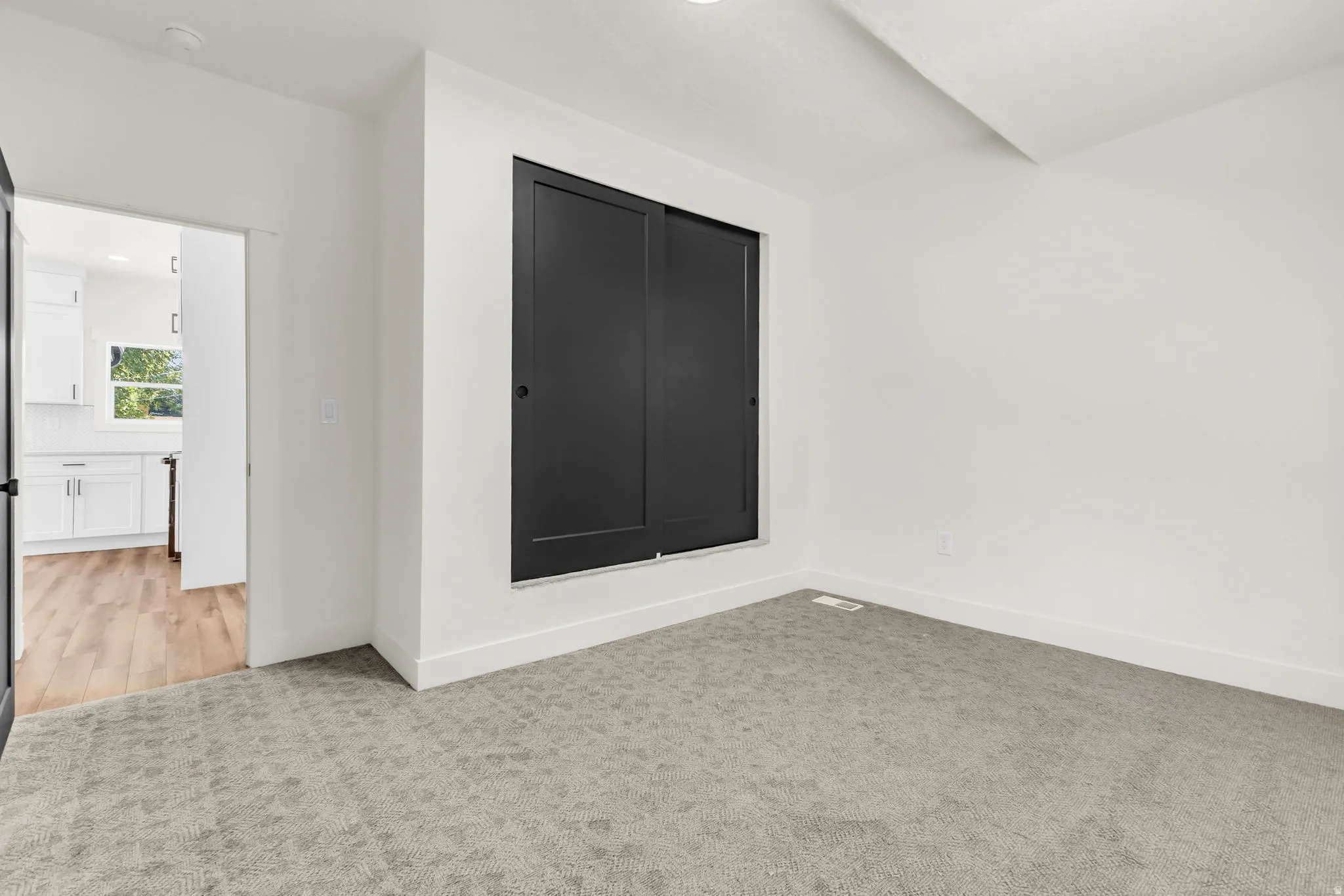 Bright room featuring a dark sliding barn door, light grey patterned carpet, and white baseboards