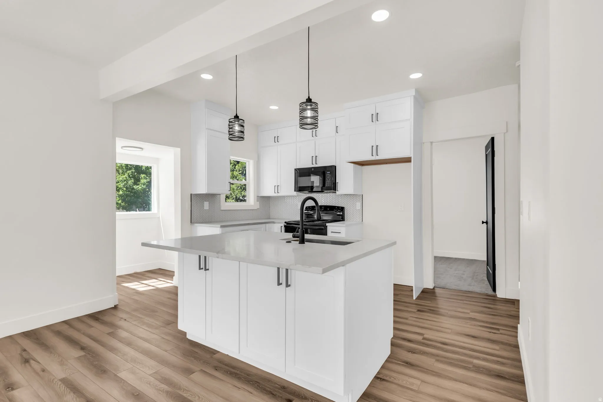 Contemporary kitchen featuring an island with a built-in sink, white cabinetry with dark hardware, a black appliance suite, and light-toned countertops