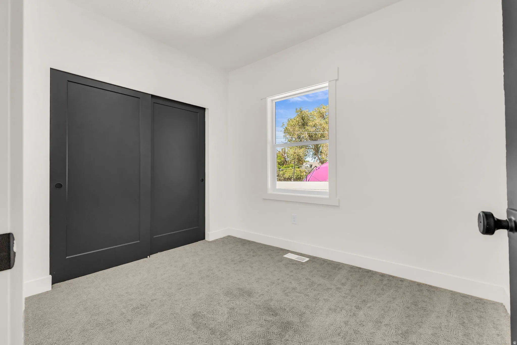 Room featuring plush grey carpeting, white painted walls, white baseboards, and a single window with white trim