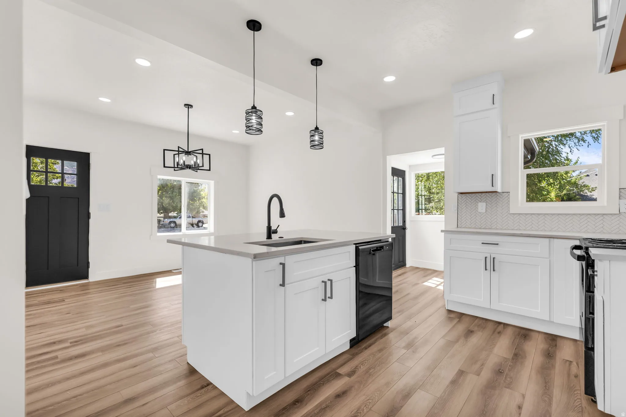 Modern kitchen featuring a central island with integrated sink, white cabinetry, sleek black appliances, and pendant lighting