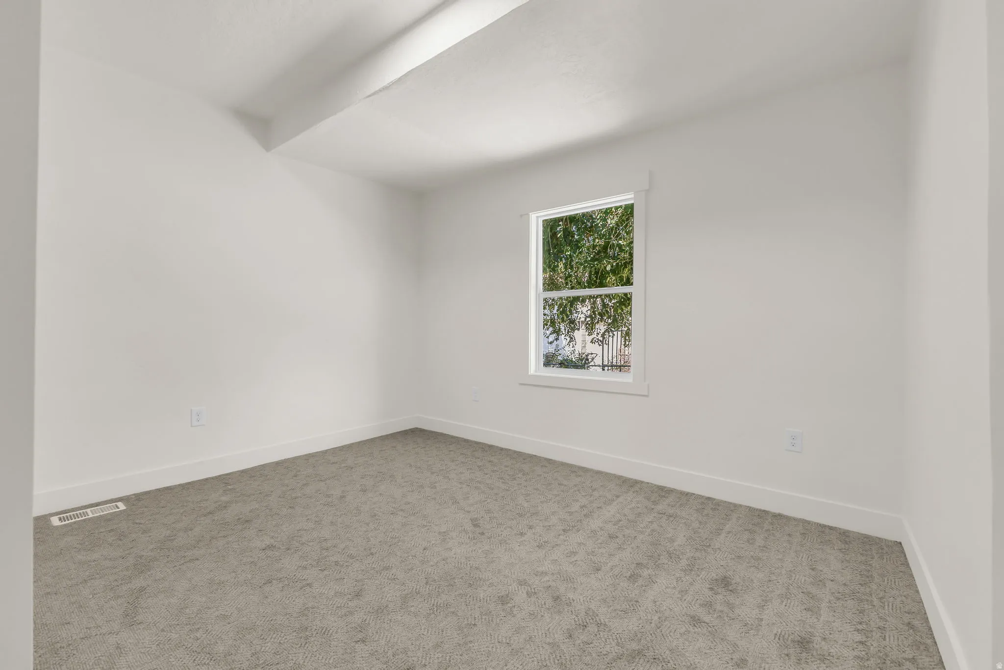 Bright room featuring a window with white trim, gray carpet, white walls, and white baseboards