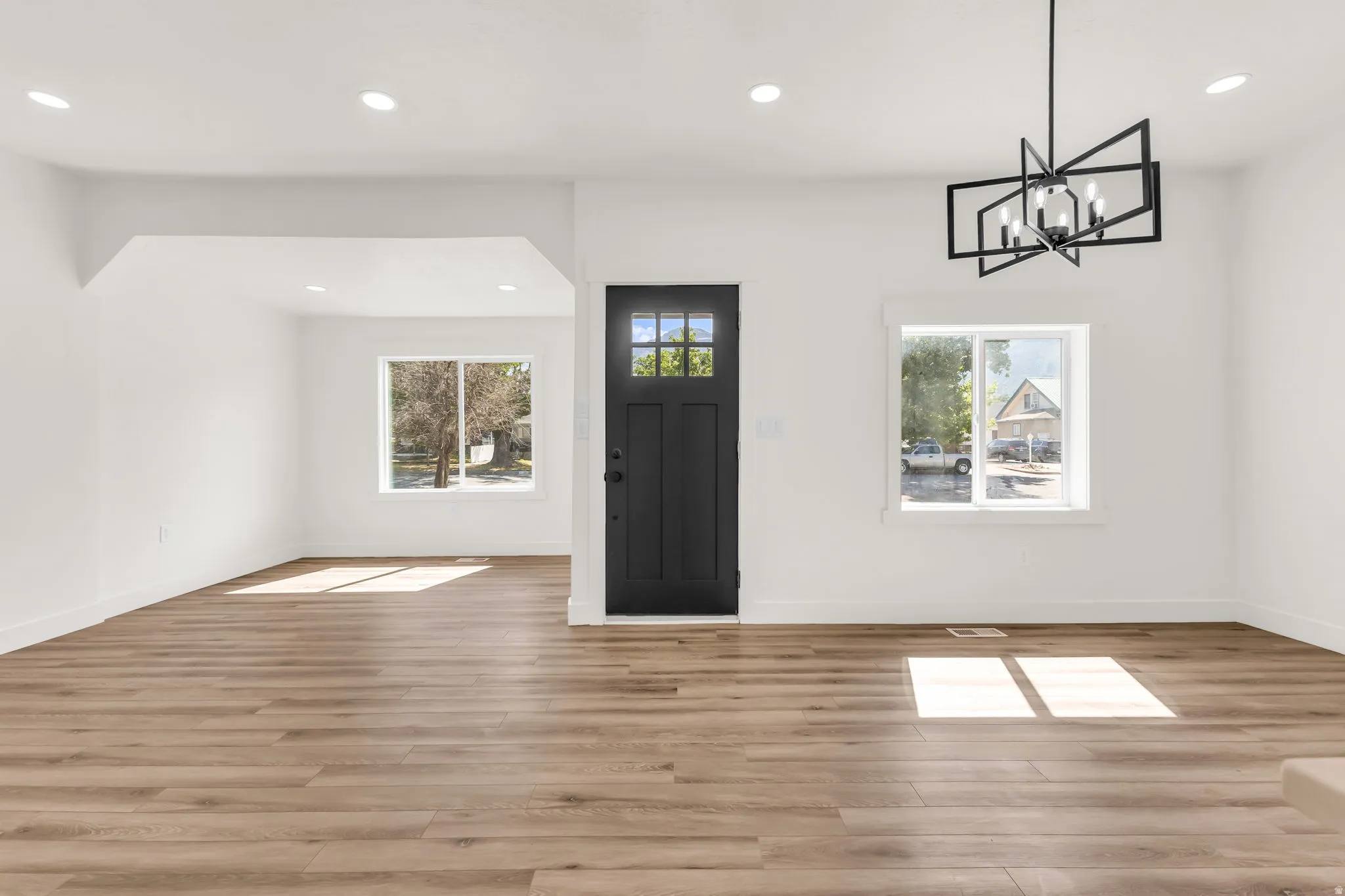 Open-concept living space with wood-finish flooring, recessed lighting, and a modern geometric chandelier