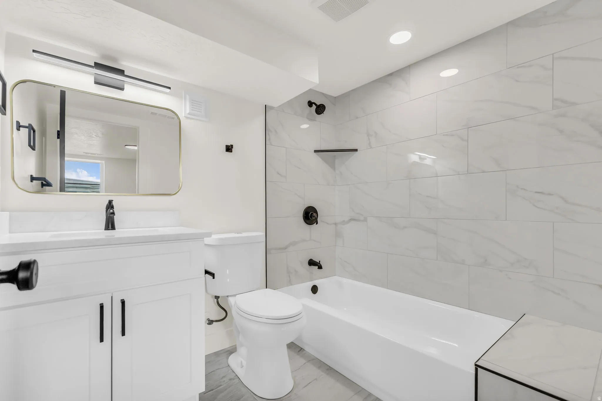 Modern bathroom featuring a white vanity with matte black hardware, a rectangular gold-framed mirror, and a sleek black light fixture