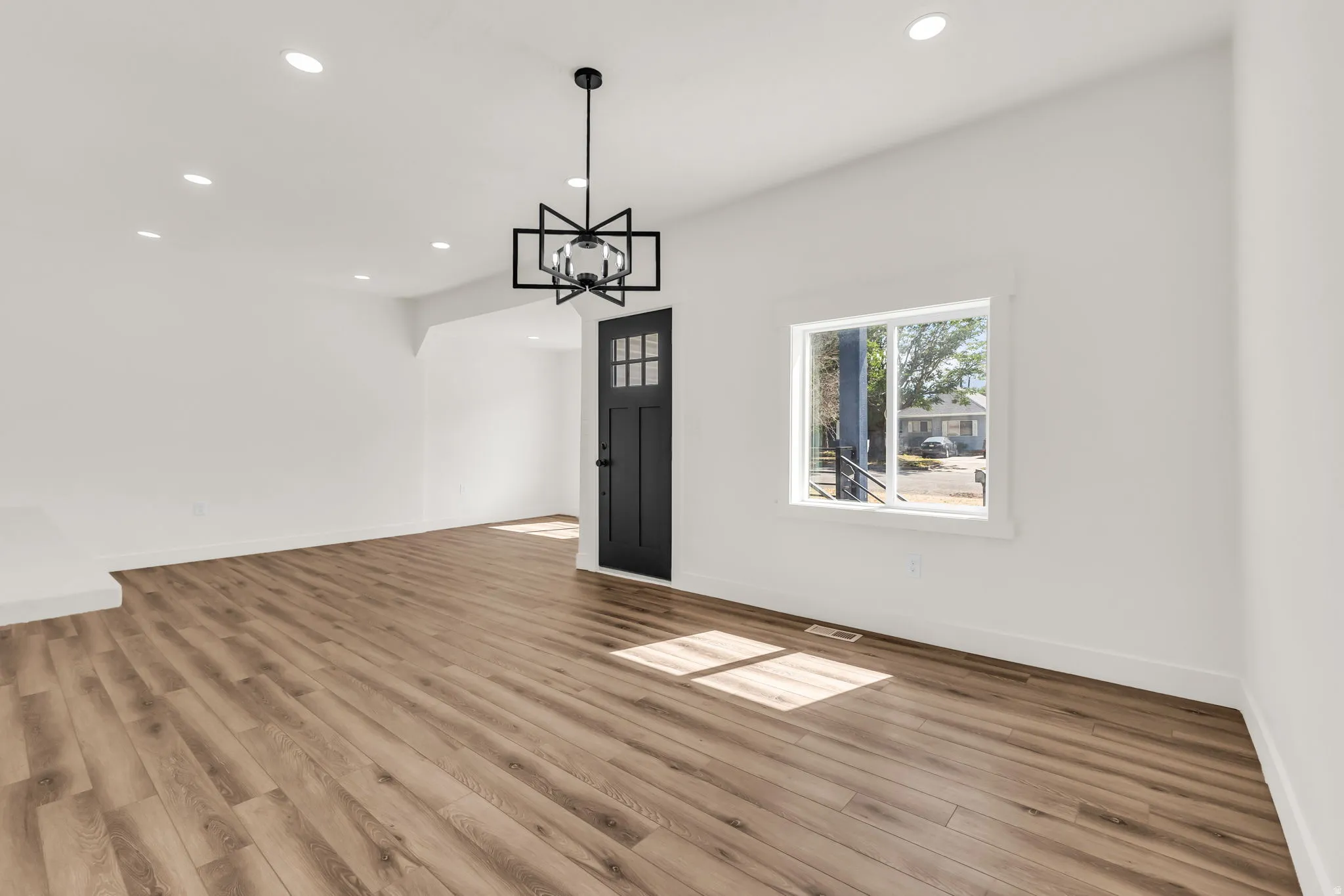 Spacious room featuring wood-finish flooring, recessed lighting, and a modern geometric chandelier