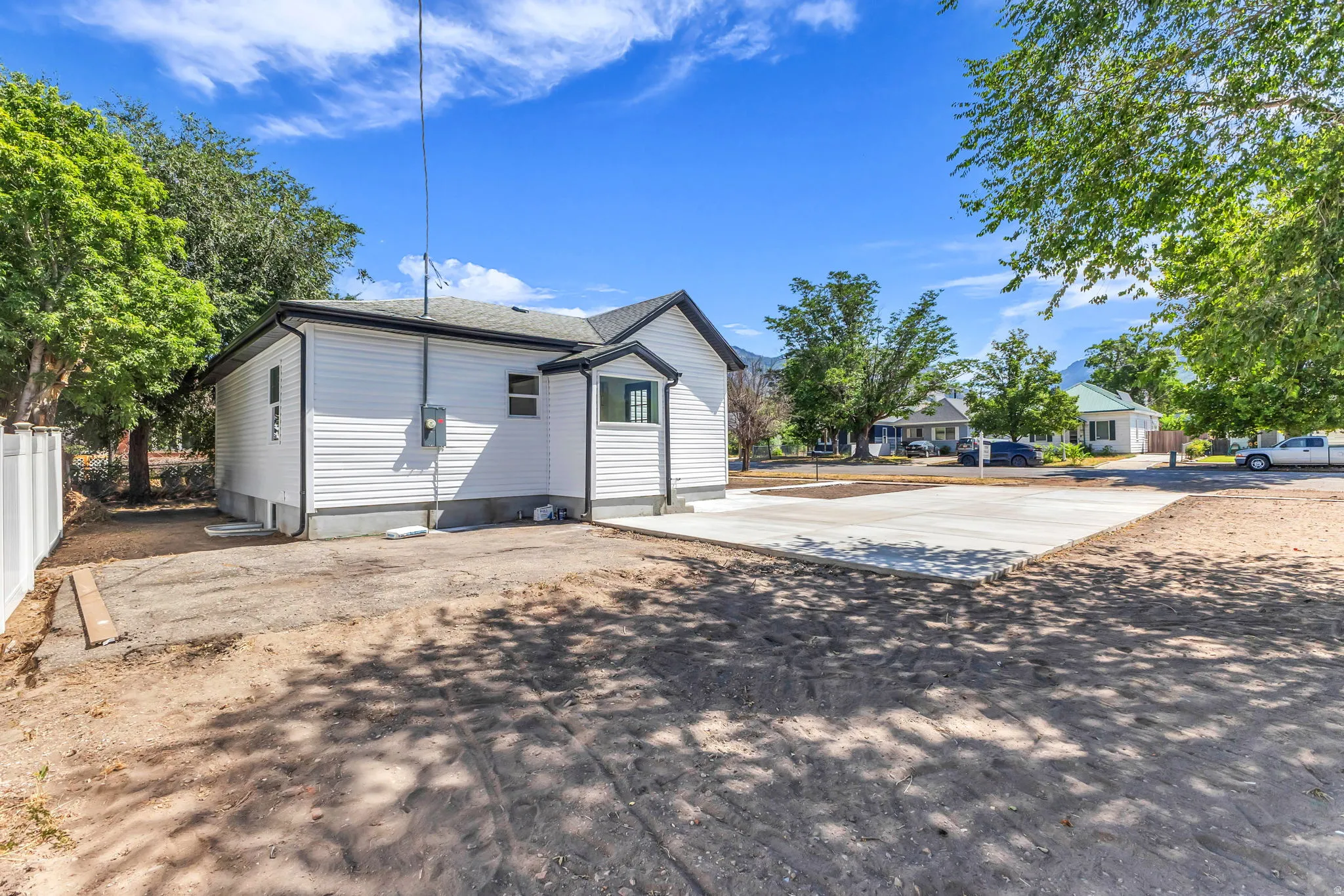 White siding exterior with a dark roof and trim, featuring a newly poured concrete pad