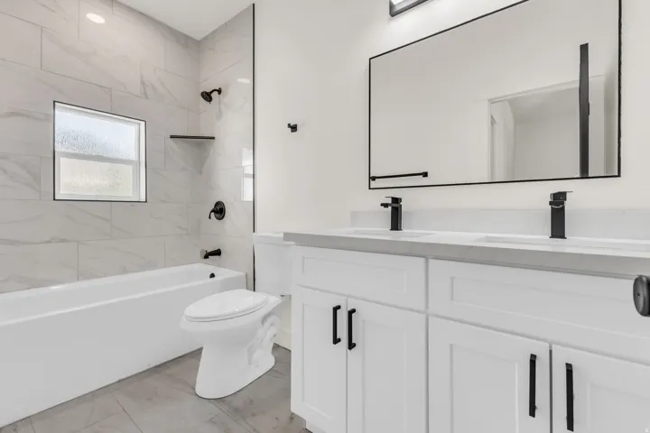 Modern bathroom featuring a dual vanity with white shaker-style cabinetry, matte black fixtures, and a large framed mirror