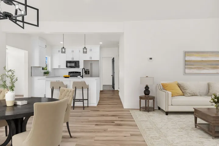 Open-concept living space featuring wood-finish flooring, a contemporary kitchen island with seating, pendant lighting fixtures, and a modern black geometric chandelier