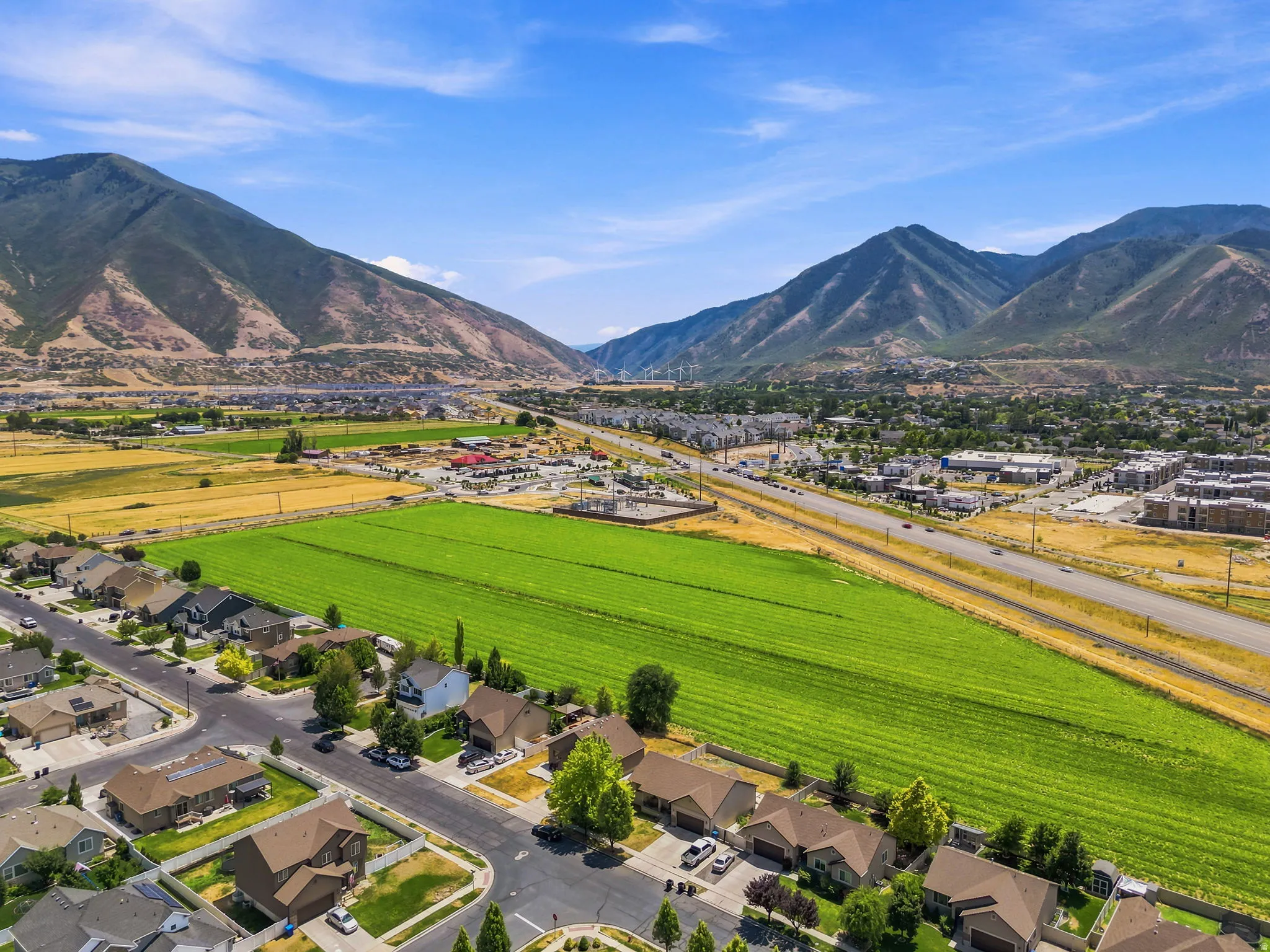 Expansive green fields bordering a residential neighborhood with distant mountain ranges under a clear sky