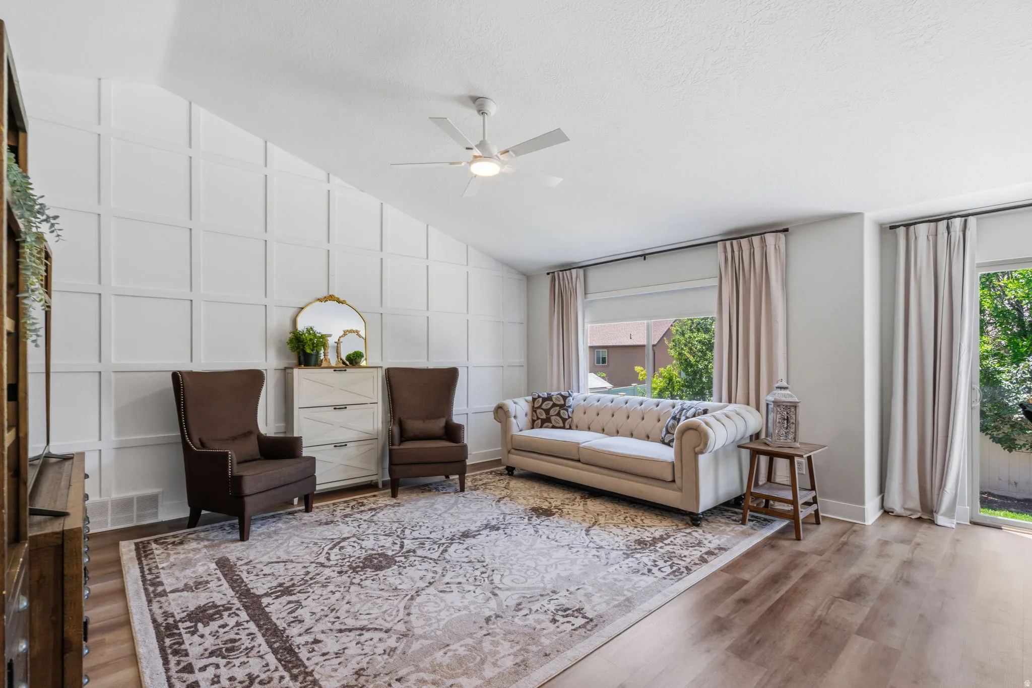 Vaulted ceiling with a ceiling fan, wall paneling, and wood-finish flooring