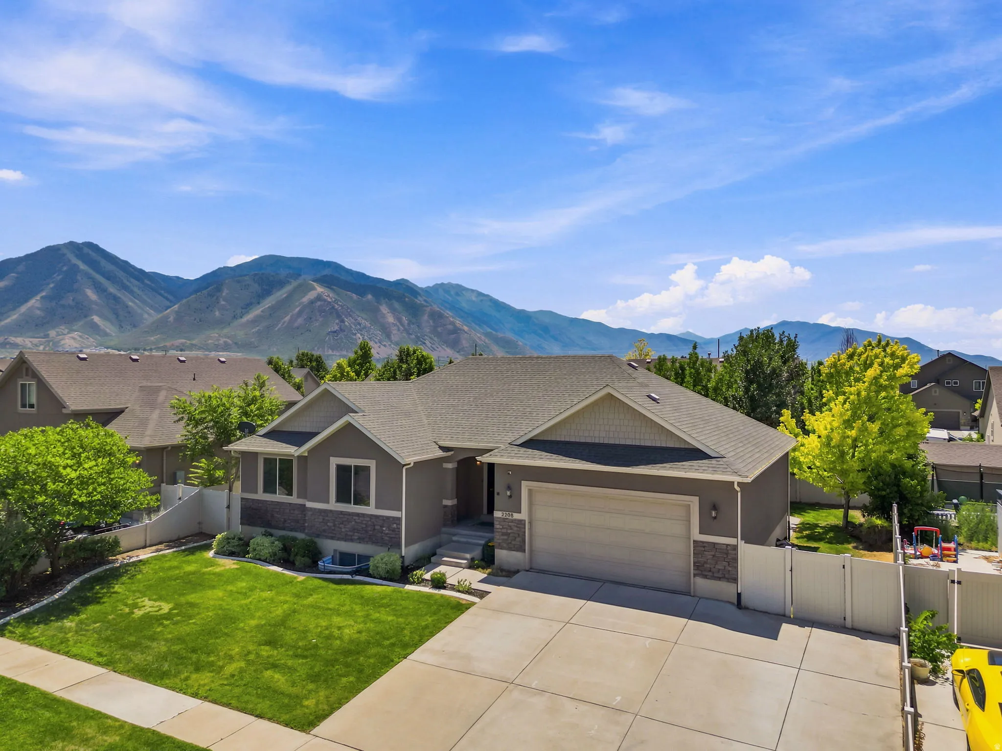 Contemporary home with a stone and siding exterior, a two-car garage, manicured front lawn, and a mountain backdrop