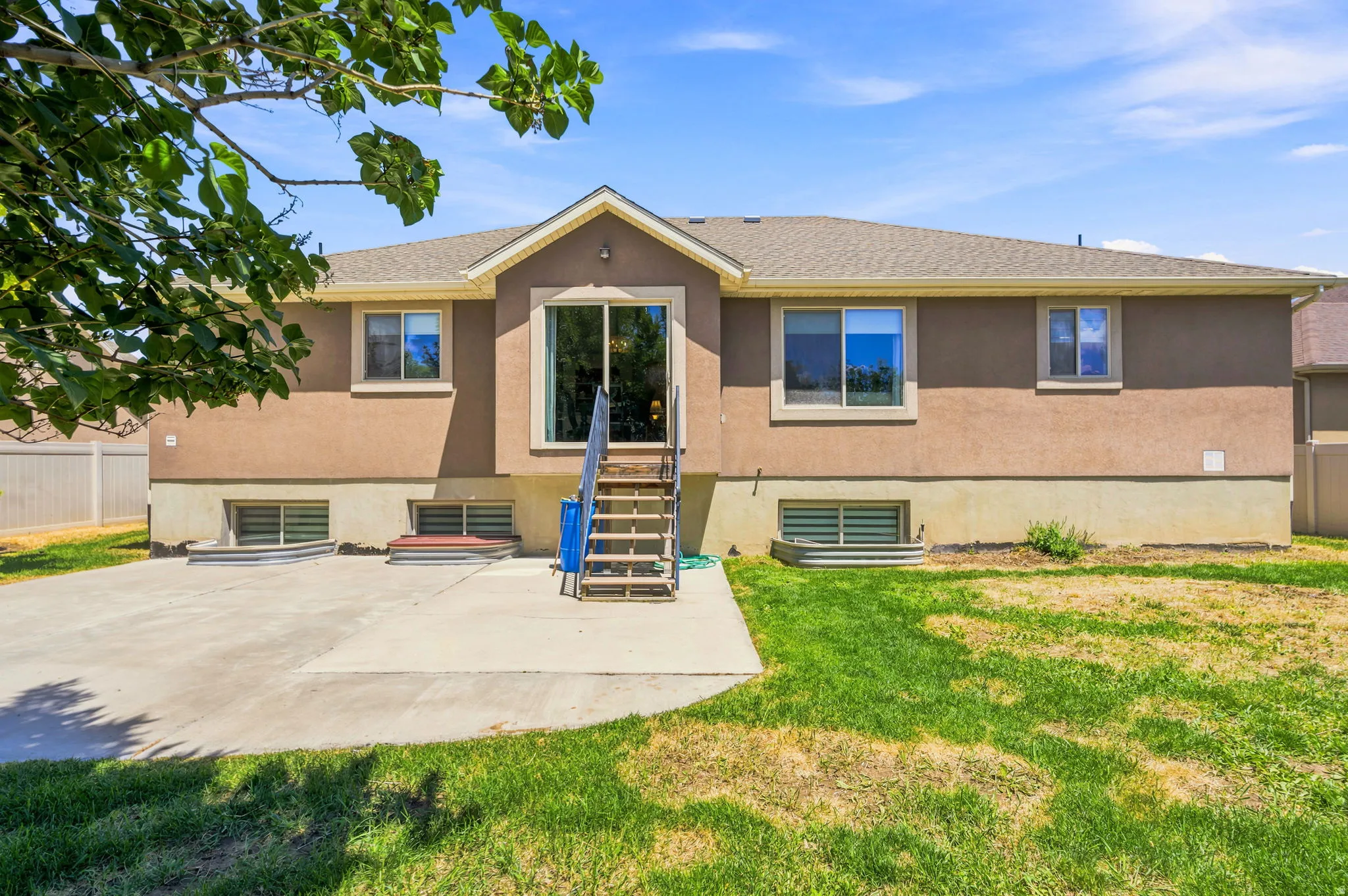Rear exterior featuring a brown stucco finish, concrete patio, and a grass area