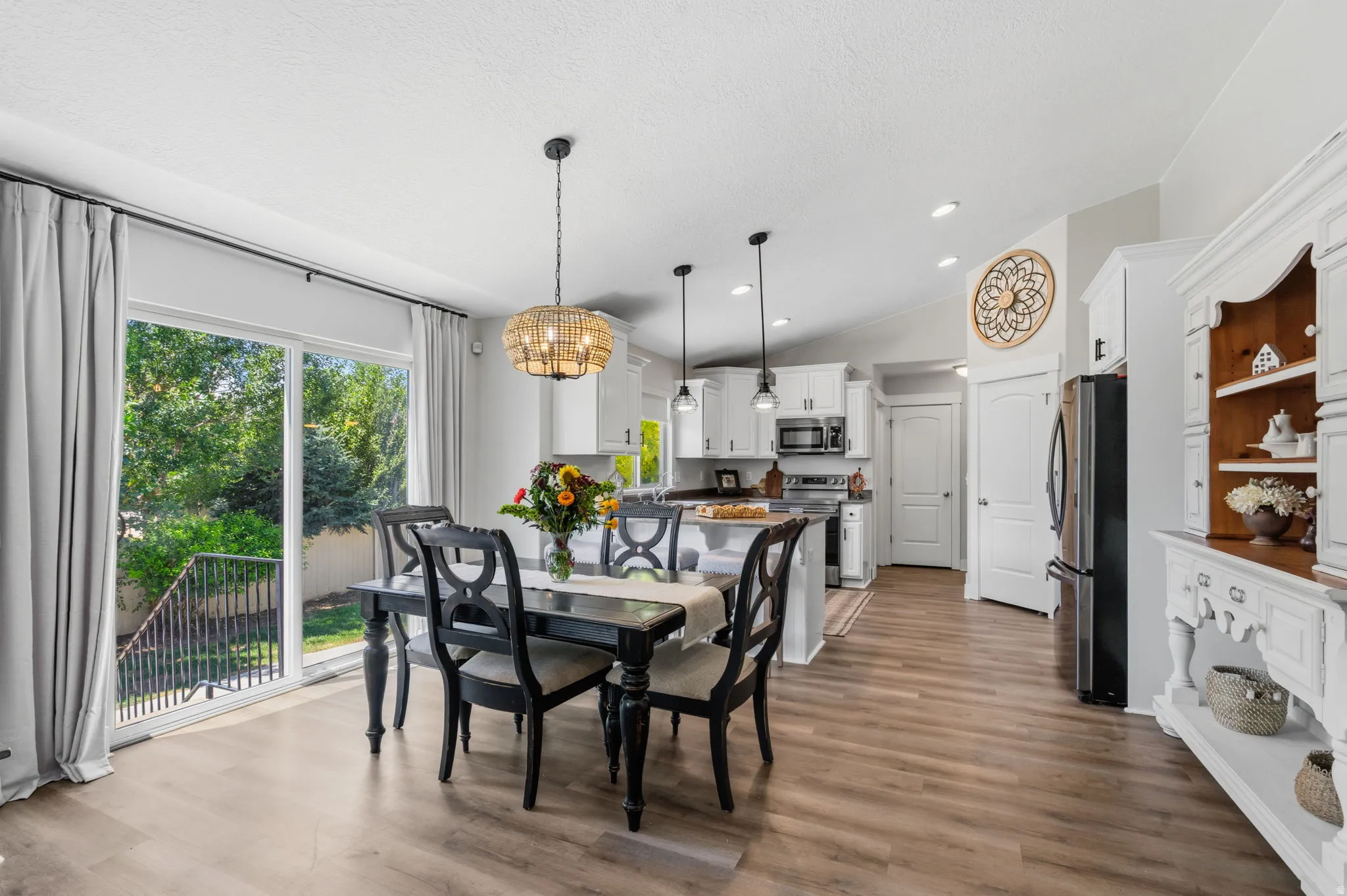 Open-concept living space featuring wood-finish flooring, a white kitchen with stainless steel appliances, and a dining area with a modern chandelier