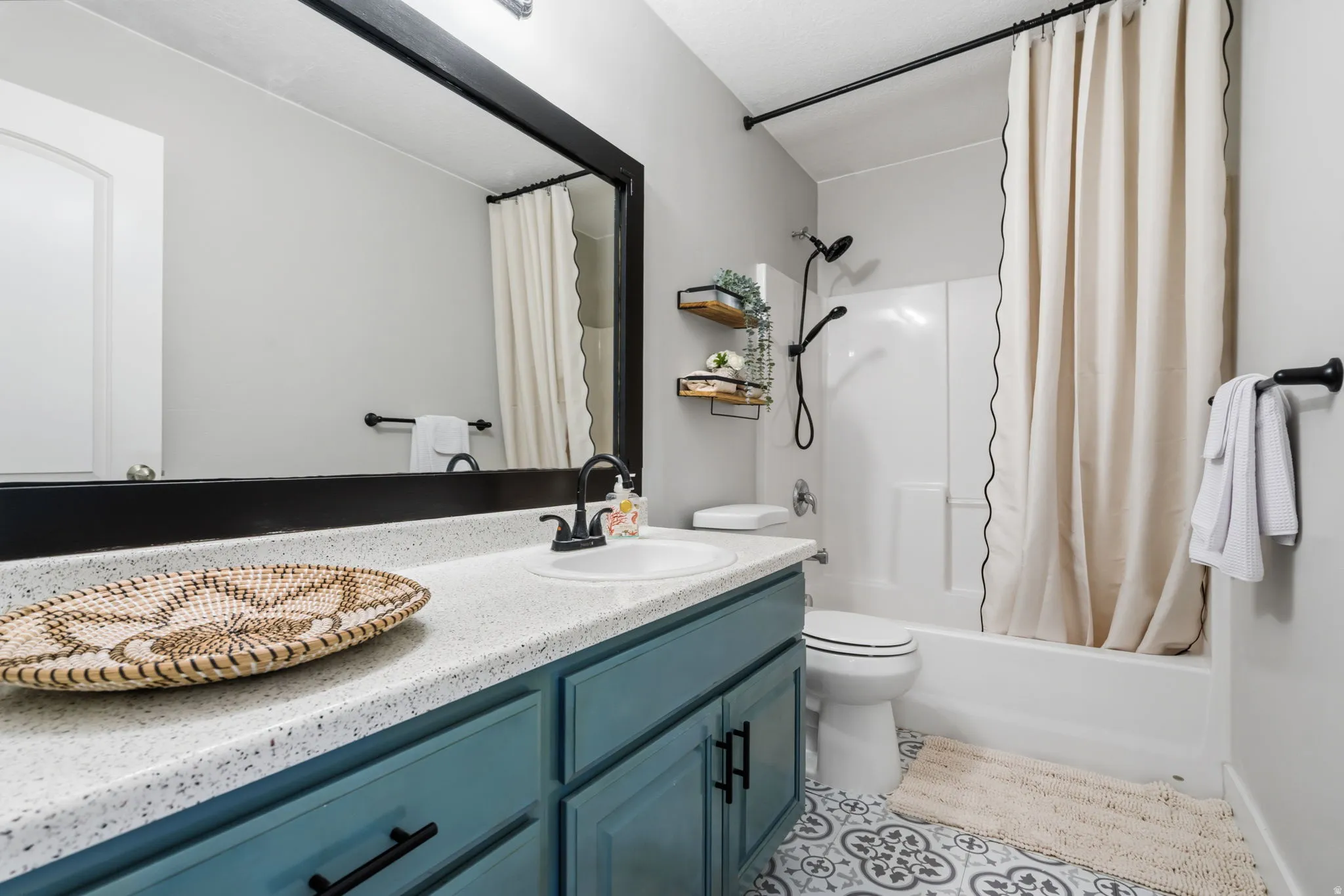 Bathroom featuring a teal vanity with a speckled countertop, a large framed mirror, and a shower-over-tub combination with a white surround