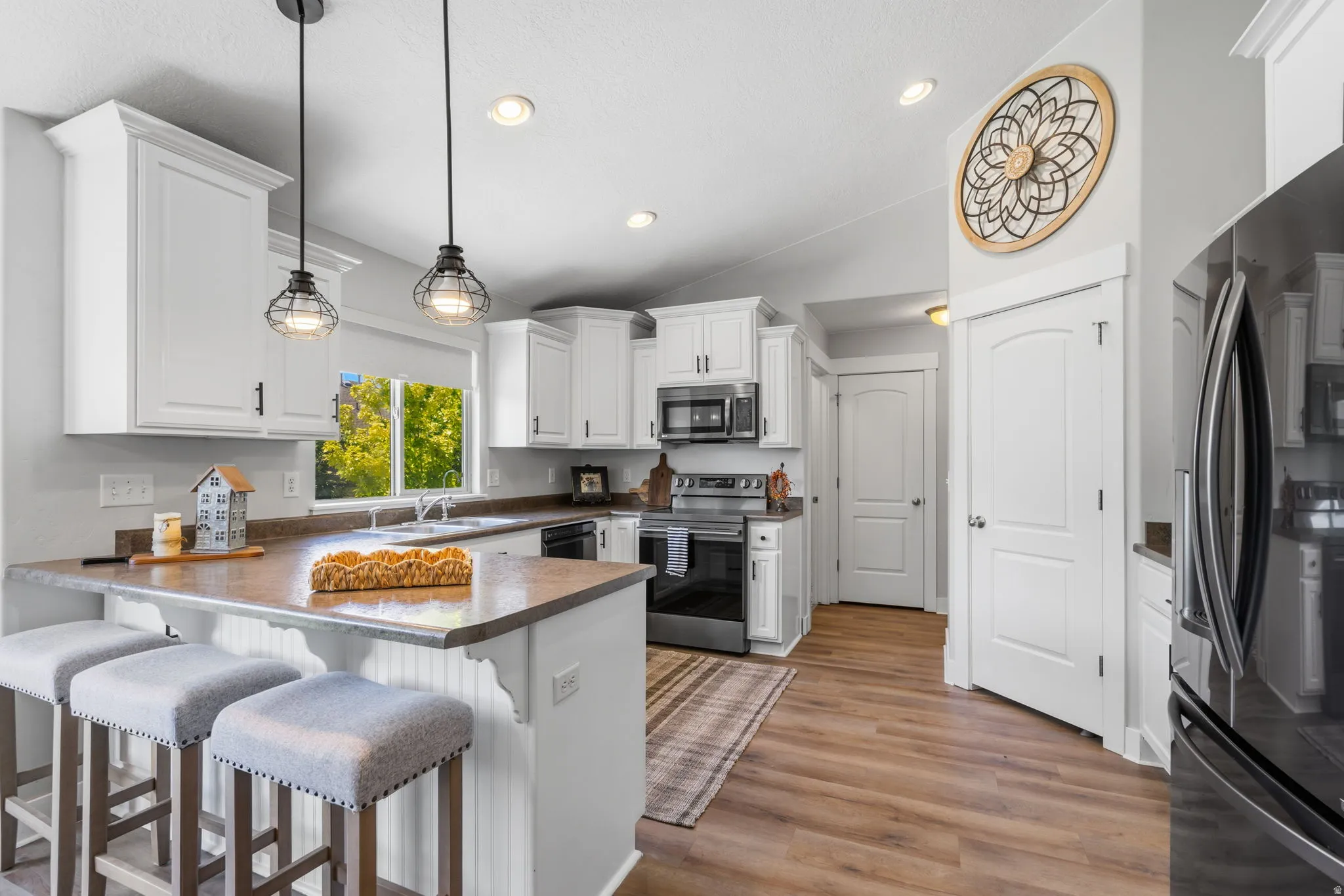 Modern kitchen featuring white cabinetry, stainless steel appliances, a breakfast bar with pendant lighting, wood-finish flooring, and a built-in pantry