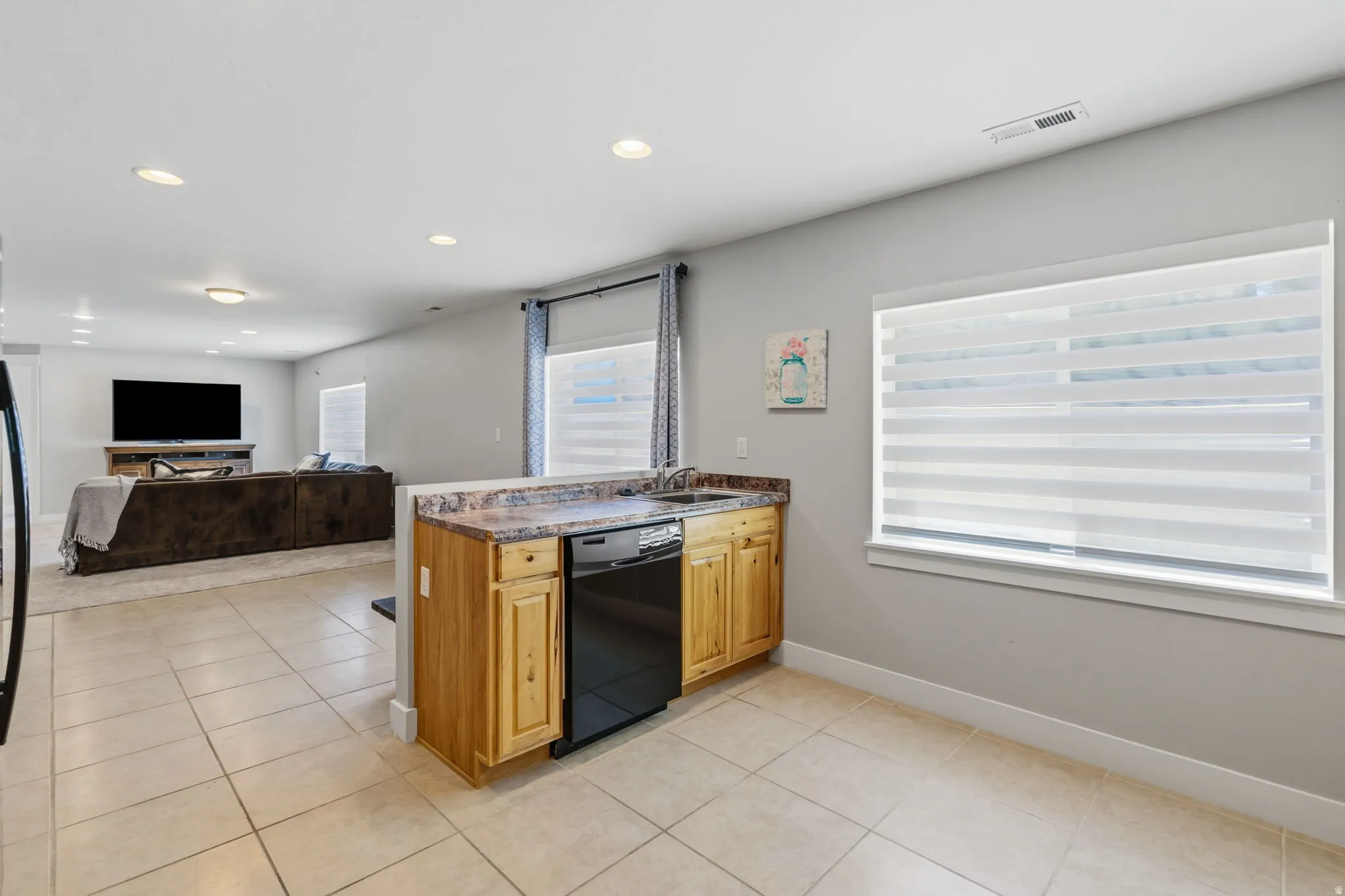 Kitchen featuring light wood cabinetry, a black dishwasher, and a laminate countertop with an integrated sink