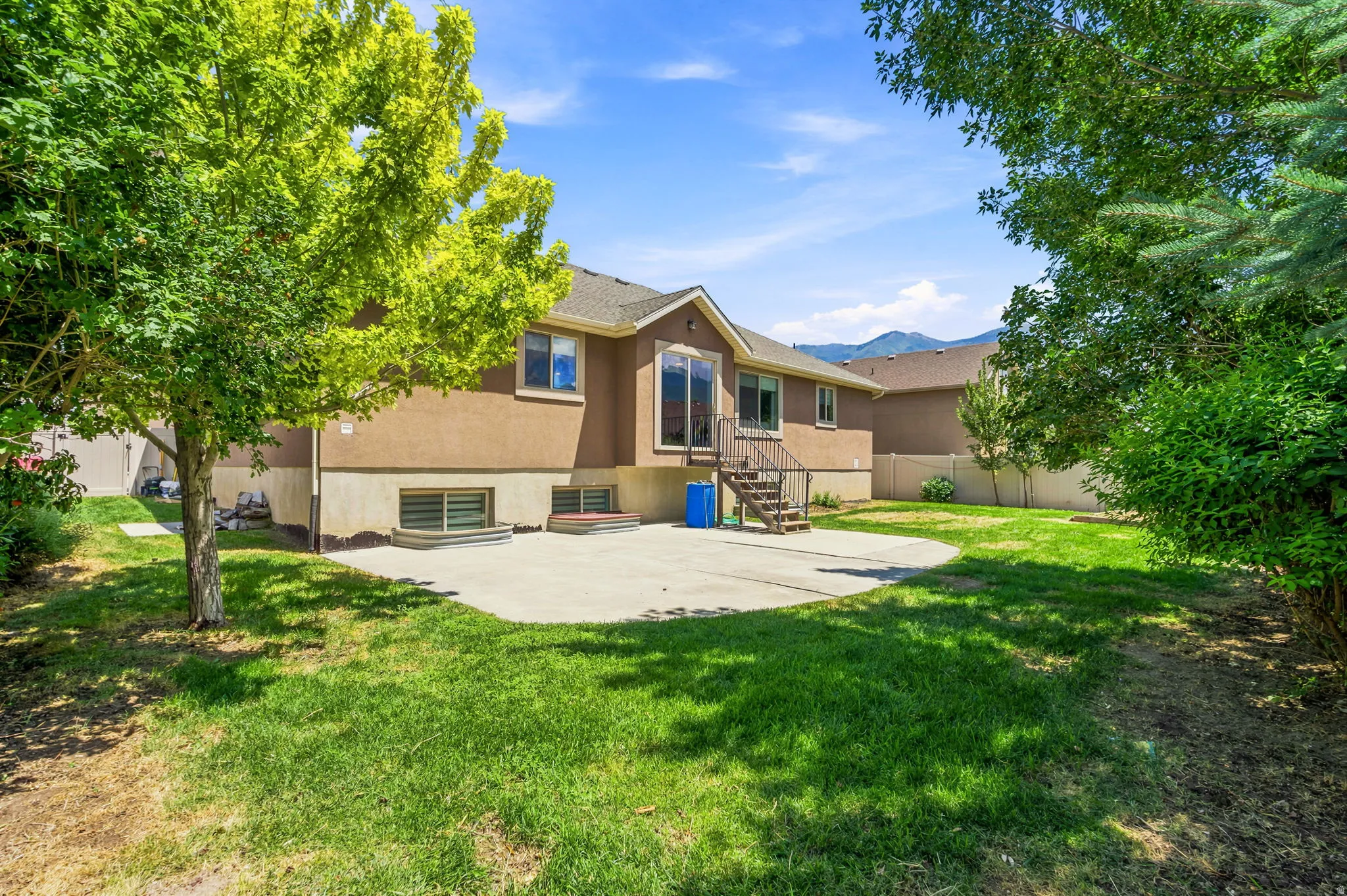 Expansive backyard featuring a concrete patio, mature trees, and a terraced lawn