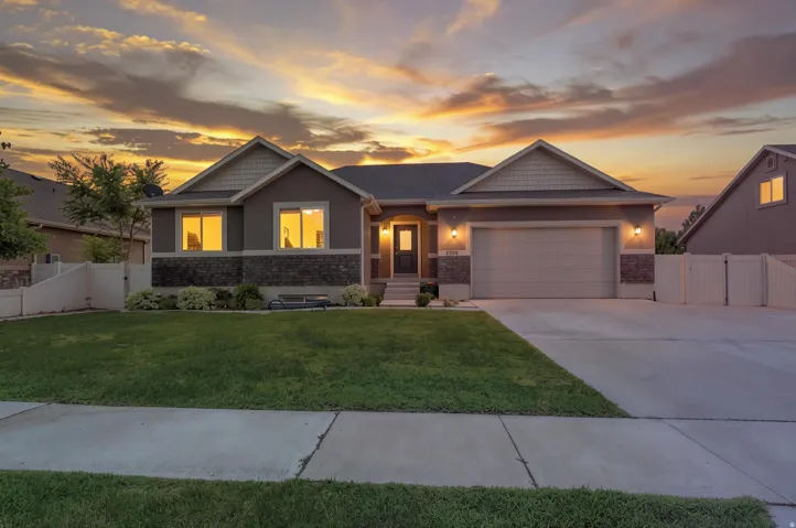Contemporary residence featuring a two-car garage, stone and stucco exterior, gabled rooflines, concrete driveway, and a front lawn with foundational landscaping