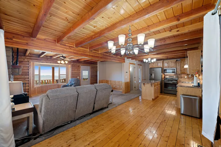 Open-concept living space featuring wood-finish flooring, exposed beam ceiling, and a kitchen with stainless steel appliances