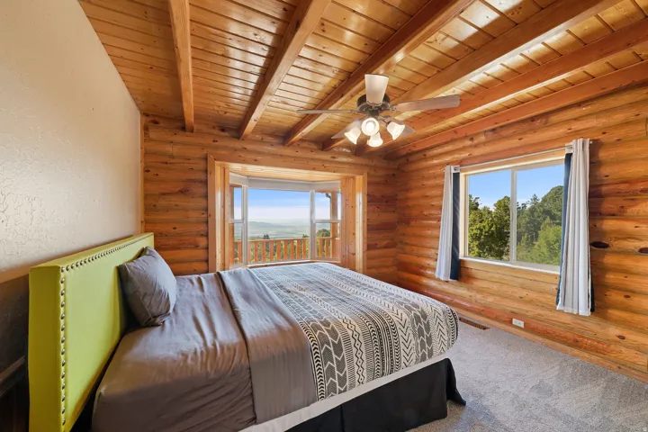 Room featuring log walls, wood-finish ceiling with exposed beams, and a ceiling fan with integrated lighting