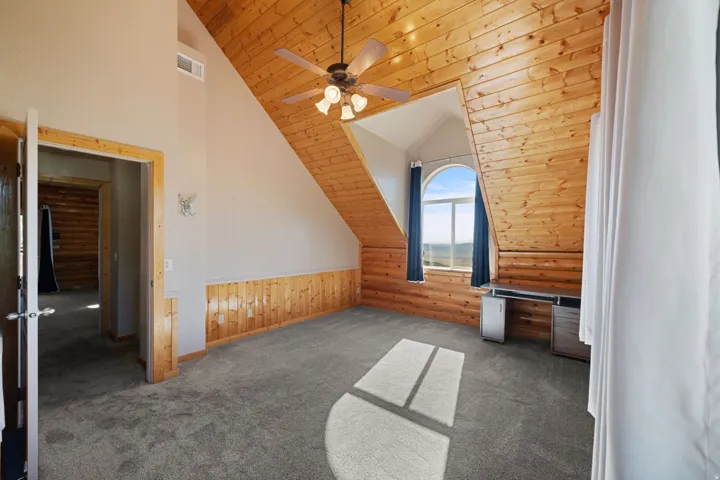 Spacious interior featuring a vaulted wood-paneled ceiling, coordinating wood wainscoting, and gray carpet flooring