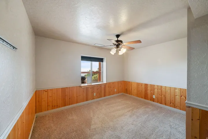 Room featuring wainscoting, a window with a wide sill, a ceiling fan with integrated lighting, and neutral-toned carpeting