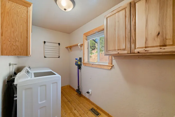 Utility area featuring wood-finish flooring, light wood cabinetry, and a single window with natural wood trim