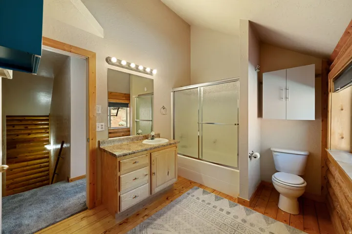 Bathroom featuring a single vanity with a laminate countertop, a mirrored medicine cabinet, a shower-over-tub with sliding glass doors, and light wood-finish flooring