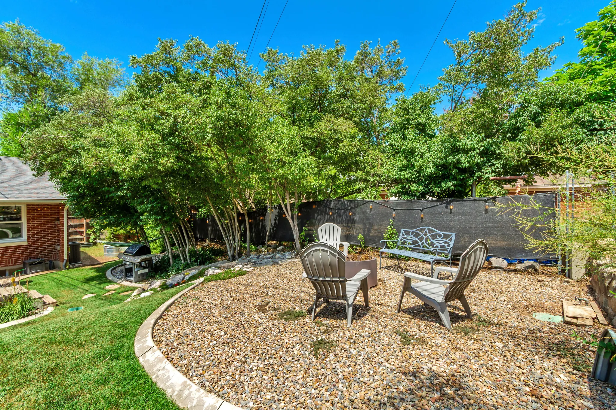 Outdoor living area featuring a gravel patio, mature trees, and a privacy screen