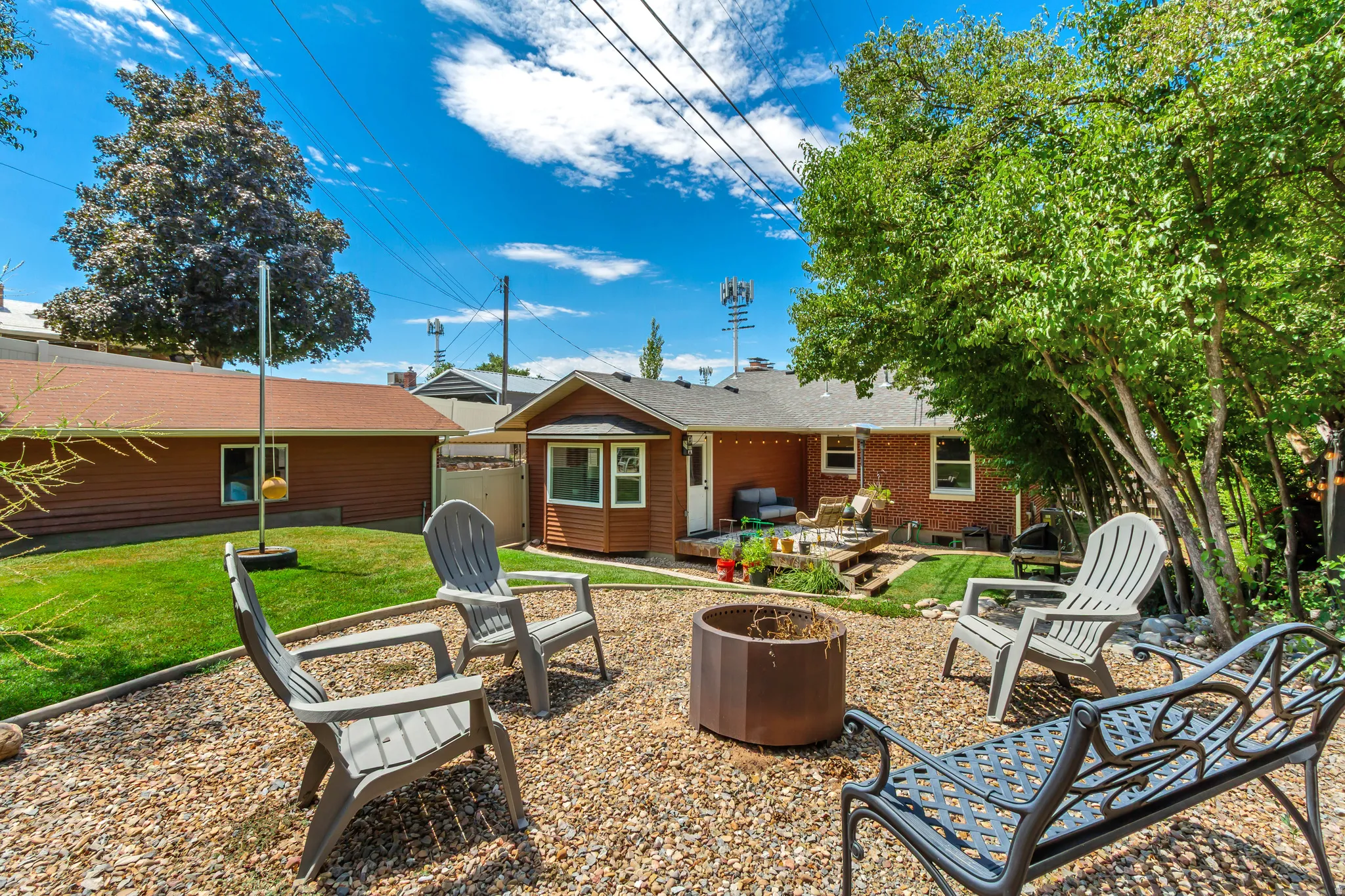 Spacious backyard featuring a gravel patio with a metal fire pit, a tiered lawn area, and mature trees providing shade