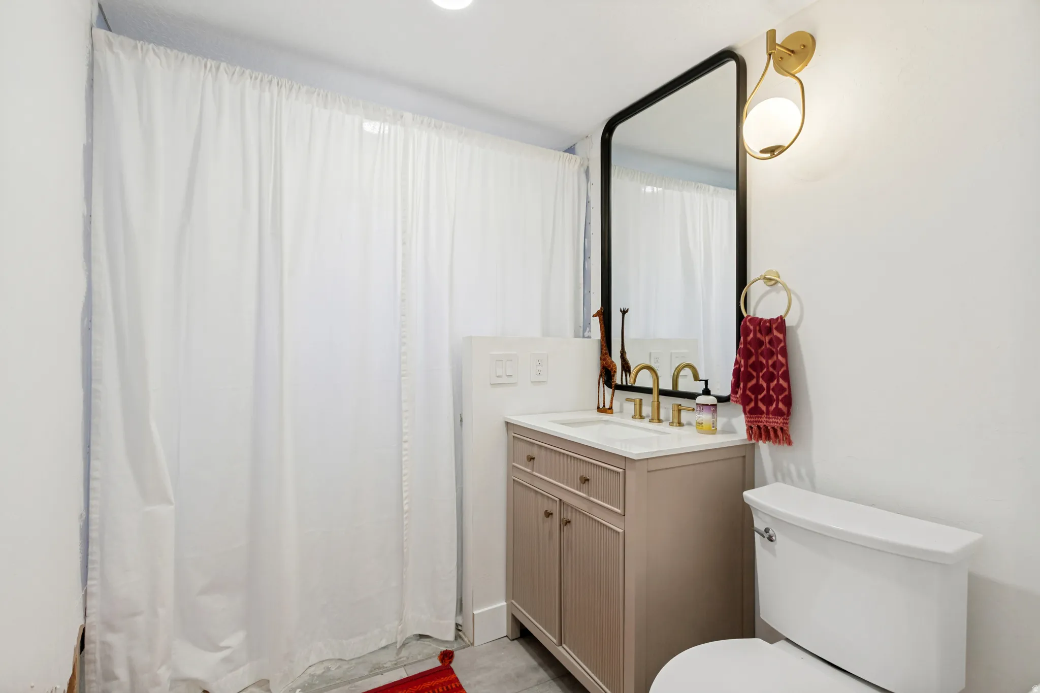 Bathroom vanity with a white countertop, brass-finish faucet, and a black-framed rectangular mirror