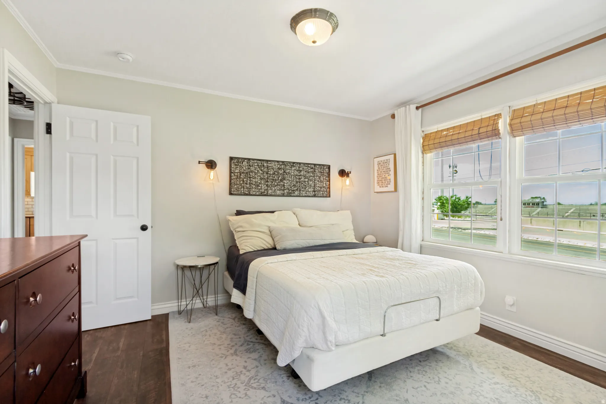 Bright bedroom featuring wood-finish flooring, white trim, and a ceiling-mounted light fixture