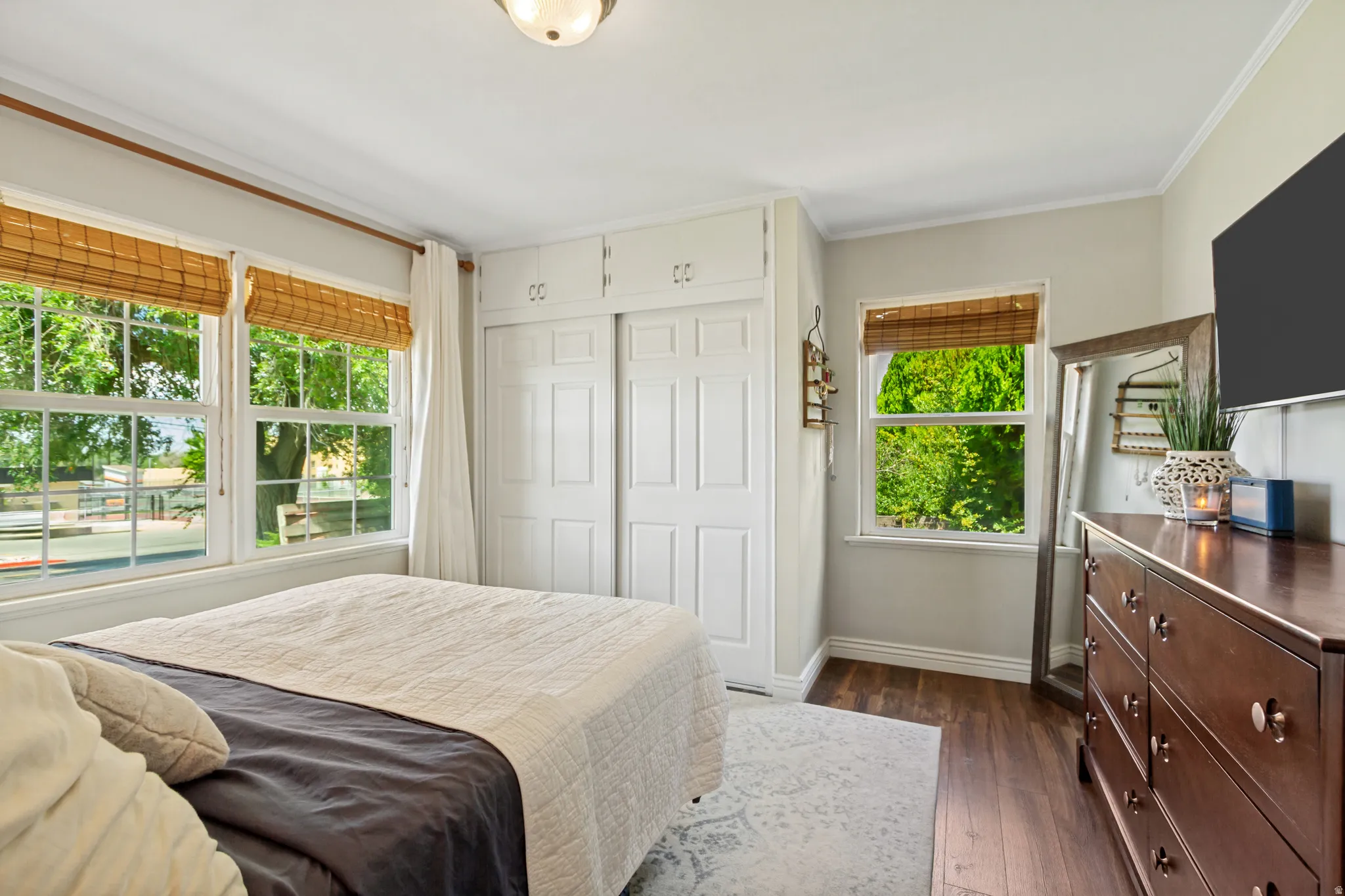 Bedroom featuring wood-finish flooring, multiple windows with blinds, built-in wardrobe with sliding doors, and crown molding