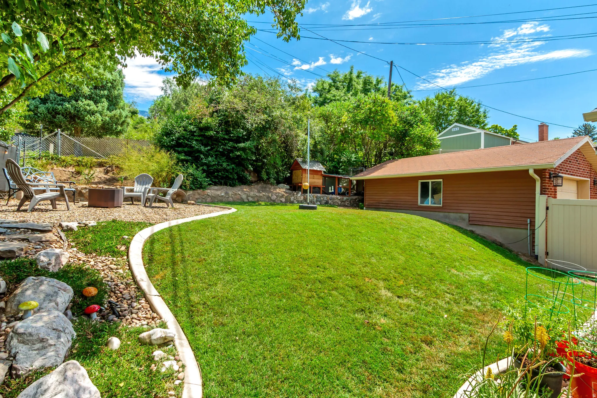 Expansive rear yard featuring a sloped lawn, a gravel patio area with stone steps, mature trees, and a privacy fence
